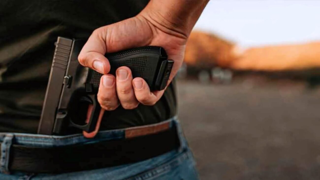 Homem retirando a pistola de dentro da calça.